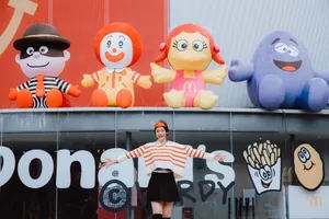 Woman posing happily in front of colorful inflatable fast food characters, radiating playful energy. jigsaw puzzle