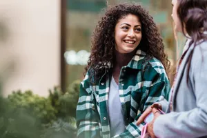 Cheerful woman with long curly hair in casual clothes standing and communicating with friend on street in daylight jigsaw puzzle