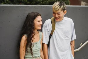 Smiling multiracial couple in casual clothes standing near stone fence on street in daylight jigsaw puzzle
