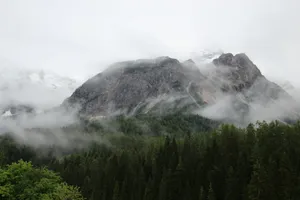 A mountain covered in clouds with trees in the foreground jigsaw puzzle