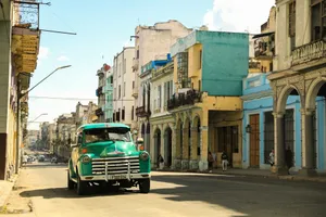 a green truck driving down a street next to tall buildings jigsaw puzzle