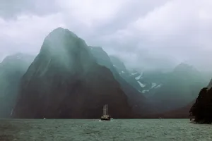 A sailboat navigating the dramatic and cloudy landscape of Milford Sound. jigsaw puzzle