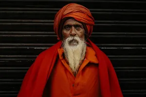 Elderly man with white beard in bright orange robe and turban stands against a dark background. jigsaw puzzle
