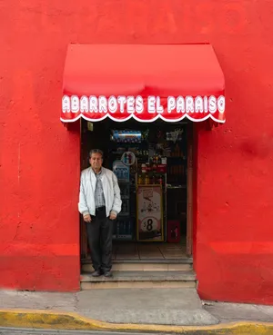 Senior man stands at the entrance of a vibrant red grocery store in a city. jigsaw puzzle