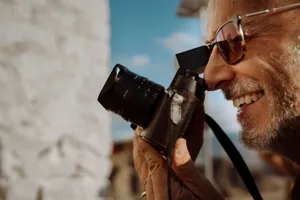 Close-up of a smiling man taking a photo with a vintage camera outdoors. jigsaw puzzle