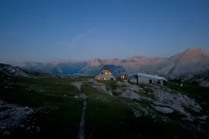 A serene alpine hut in the Austrian mountains at twilight, glowing warmly against rugged peaks. jigsaw puzzle