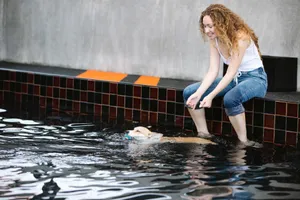 Content female taming intelligent purebred dog with ball in mouth swimming in rippled water against tiled wall jigsaw puzzle