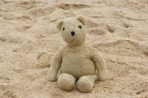 A lone teddy bear sits on a sandy beach, evoking nostalgia and childhood memories. jigsaw puzzle