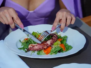Woman enjoying an octopus salad with fresh greens outdoors. Vibrant and appetizing. jigsaw puzzle