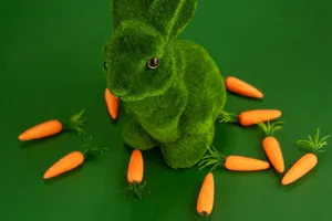 A fuzzy green rabbit figurine surrounded by miniature carrots on a green background. jigsaw puzzle