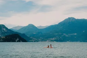 Two people kayaking on a tranquil lake surrounded by scenic mountains under a cloudy sky. jigsaw puzzle