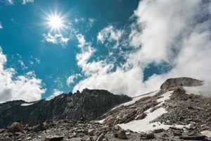 Rugged mountain terrain with snow patches under a bright sun and vibrant blue sky. jigsaw puzzle