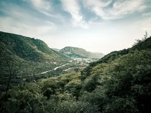 A breathtaking view of green hills with a small town nestled between them under a clear sky. jigsaw puzzle