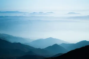 A tranquil scene of misty mountain ranges under a soft, blue sky at sunrise. jigsaw puzzle