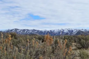 Explore the scenic view of snow-capped mountains and wilderness under a cloudy sky. jigsaw puzzle