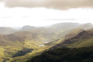 Aerial view of lush green mountains and valleys under a cloudy sky, showcasing natural beauty. jigsaw puzzle