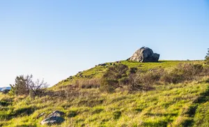Peaceful landscape featuring a green hill, large rock, and vast clear sky. jigsaw puzzle