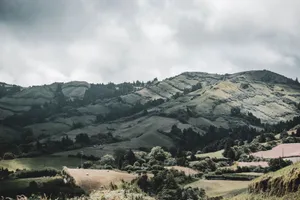 Lush green hills and forests under a cloudy sky create a serene mountain landscape. jigsaw puzzle