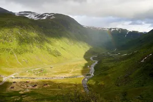Breathtaking aerial view of a lush green valley with a rainbow stretching across the mountainous horizon. jigsaw puzzle