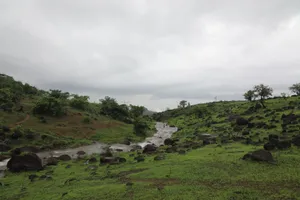 A scenic view of rolling green hills with a stream flowing through under a cloudy sky. jigsaw puzzle