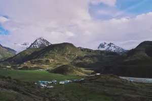 Picturesque village nestled in lush mountains with snow-capped peaks under a cloudy sky. jigsaw puzzle
