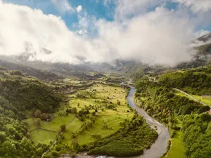 A picturesque aerial landscape of a lush green river valley, framed by clouds and mountains. jigsaw puzzle