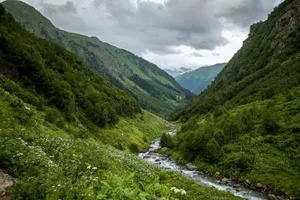 Lush green mountain valley with a winding stream under a cloudy sky in the Caucasus. jigsaw puzzle