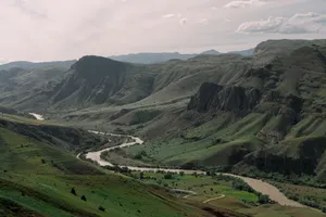 A breathtaking view of a winding river cutting through a lush green valley surrounded by majestic mountains. jigsaw puzzle