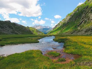 Tranquil river flowing through a lush green valley between majestic mountains under a clear blue sky. jigsaw puzzle