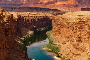 Stunning view of the Grand Canyon's rugged sandstone cliffs and serene river bend under a warm sunset. jigsaw puzzle
