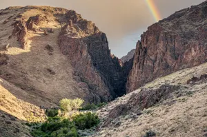 A breathtaking view of a rocky canyon landscape with a vibrant rainbow arching over a clear sky. jigsaw puzzle