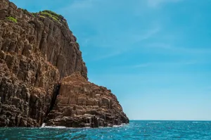 Majestic rocky cliffs meet the crystal-clear ocean under a vibrant blue summer sky. jigsaw puzzle