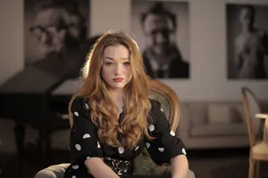 A woman with long wavy hair, seated indoors, displaying a pensive expression against a blurred background. jigsaw puzzle