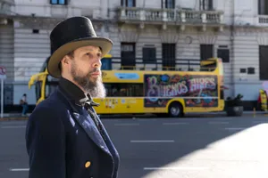 Man in 19th-century inspired attire standing near a Buenos Aires tour bus on a city street. jigsaw puzzle
