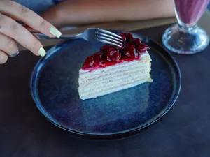 A fork held by a woman captures a cherry-topped cake slice on a blue plate, showcasing dessert indulgence. jigsaw puzzle