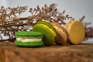 Three colorful macarons on a wooden surface with dried flowers in the background, creating a warm and vibrant scene. jigsaw puzzle
