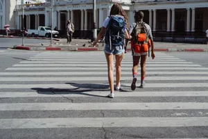 Two women with backpacks crossing a pedestrian lane in an urban setting on a sunny day. jigsaw puzzle