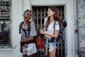 Two young women backpacking and smiling in a lively urban setting, ideal for travel-focused content. jigsaw puzzle