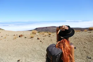 Woman standing in a desert landscape, looking at distant mountains, wearing a hat and backpack. jigsaw puzzle