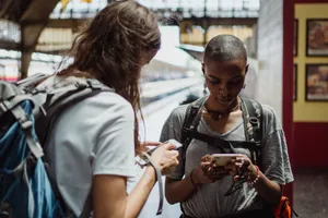 Two travelers using smartphones while waiting at a railway station, backpacks on their shoulders. jigsaw puzzle