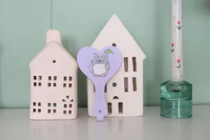 Whimsical ceramic houses and a heart-shaped ornament with a cartoon character beside a decorated candle. jigsaw puzzle
