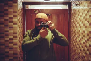 A man wearing a beanie takes a self-portrait with a vintage camera in a tiled room. jigsaw puzzle
