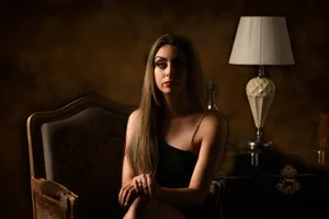 Portrait of an elegant woman seated in a dimly lit room with an ornate armchair and lamp. jigsaw puzzle