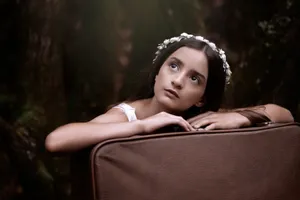 A thoughtful teenage girl wearing a floral wreath, resting on a vintage suitcase in a forest. jigsaw puzzle