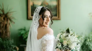 Happy bride posing with floral bouquet indoors, showcasing her elegant lace wedding dress. jigsaw puzzle