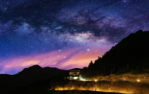 Stunning view of the Milky Way over a serene mountain landscape with a lit house at night. jigsaw puzzle