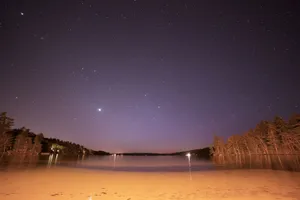 A serene night view of a beach under a starry sky with reflective waters and distant tree silhouettes. jigsaw puzzle