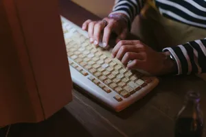 Hands typing on a vintage beige keyboard with a striped sweater visible, indoors. jigsaw puzzle