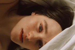 Captivating portrait of a young woman with freckles lying on a bed, enveloped in soft light. jigsaw puzzle