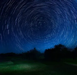 Vivid star trails creating a hypnotic pattern in a dark night sky over a tranquil outdoor landscape. jigsaw puzzle